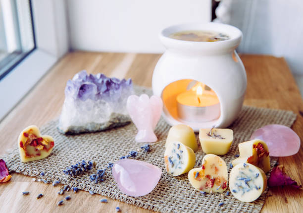 Homemade mini wax melts in aromatherapy lamp diffuser at home interior with rose quartz crystal hearts and angel for decoration on wooden window sill on winter. Seasonal spiritual zen concept.